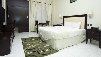 Habitación de hotel con cama, mesitas de noche, escritorio con sillas, mesa de comedor y un ventanal grande con cortinas.