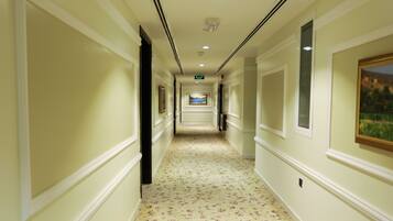 A hotel hallway with cream walls, floral carpet, framed pictures, and a ceiling light.