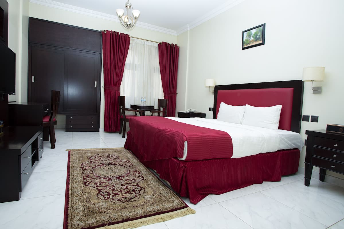 A hotel room with a large bed, a desk with a chair, a TV, a wardrobe, and a dining table with chairs.