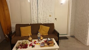 A living room with a sofa, a coffee table with flowers, a bottle of water, and books. - Beach Heaven Maldives - Golden Turtle Guest House (Huraa)