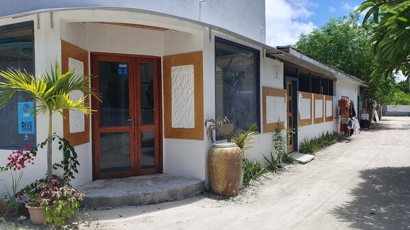 A building with a wooden door and windows, a large decorative vase, and a sign for a dive center. - Beach Heaven Maldives - Golden Turtle Guest House (Huraa)