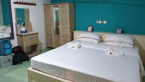 A hotel room with a bed, a wardrobe, a bedside table, a mirror, and a wall with a teal color. - Beach Heaven Maldives - Golden Turtle Guest House (Huraa)