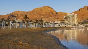 Un resort en la playa con piscina, palmeras y montañas al fondo.