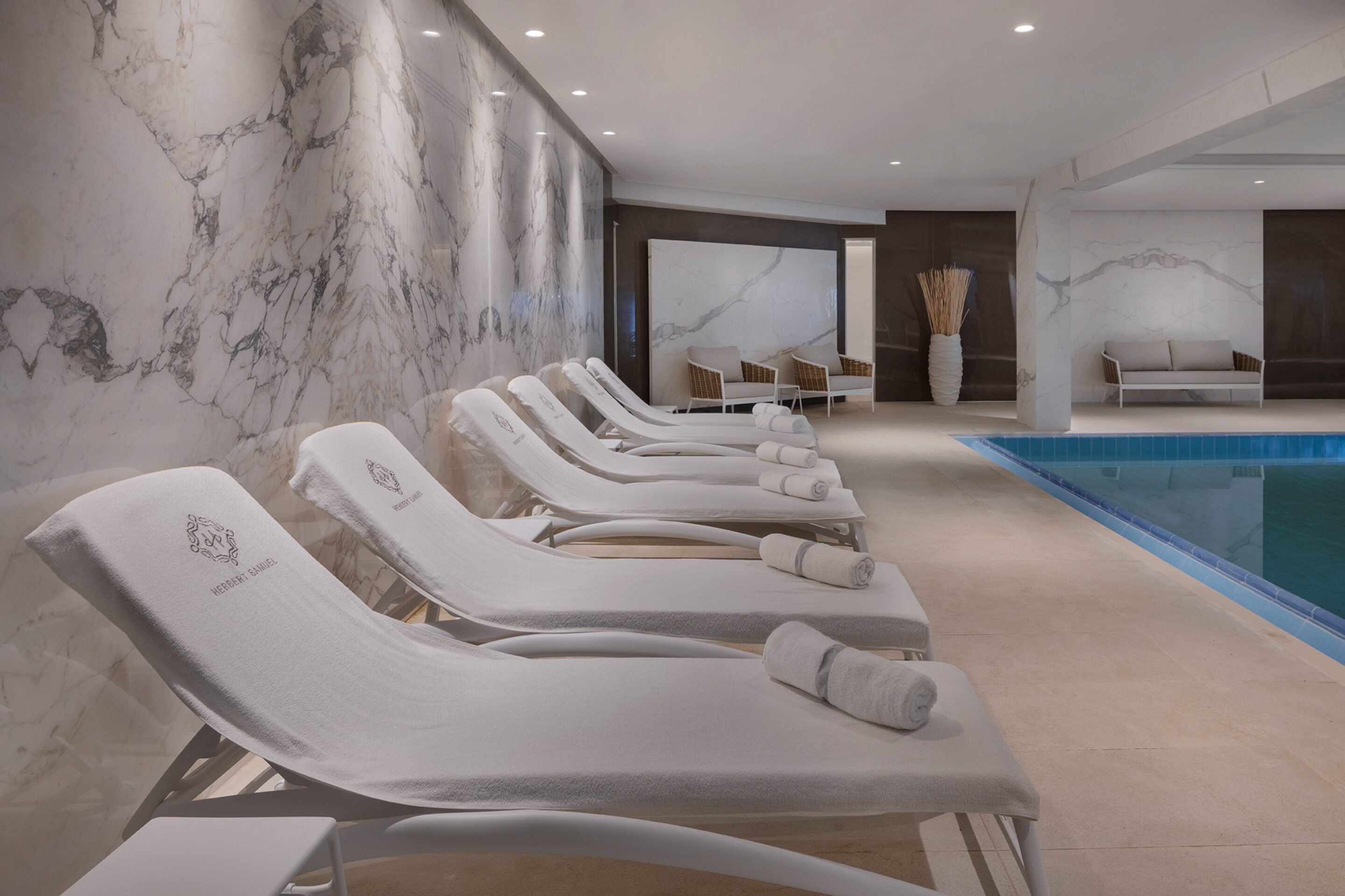 Uma área interna de piscina moderna, com cadeiras de descanso e uma grande parede com padrão de mármore.