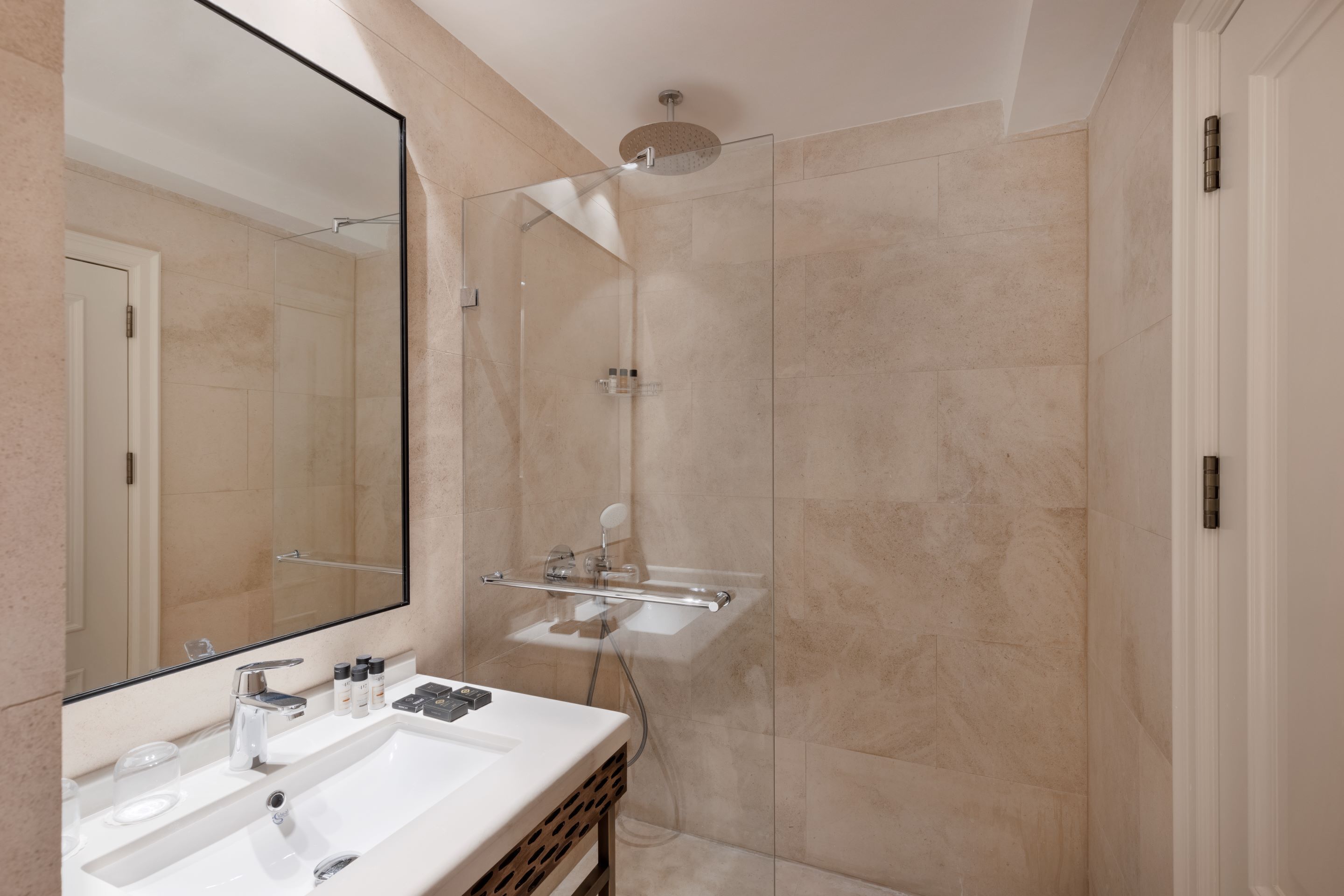 A modern bathroom with a glass-enclosed shower, a large mirror, and a vanity with a sink and toiletries.