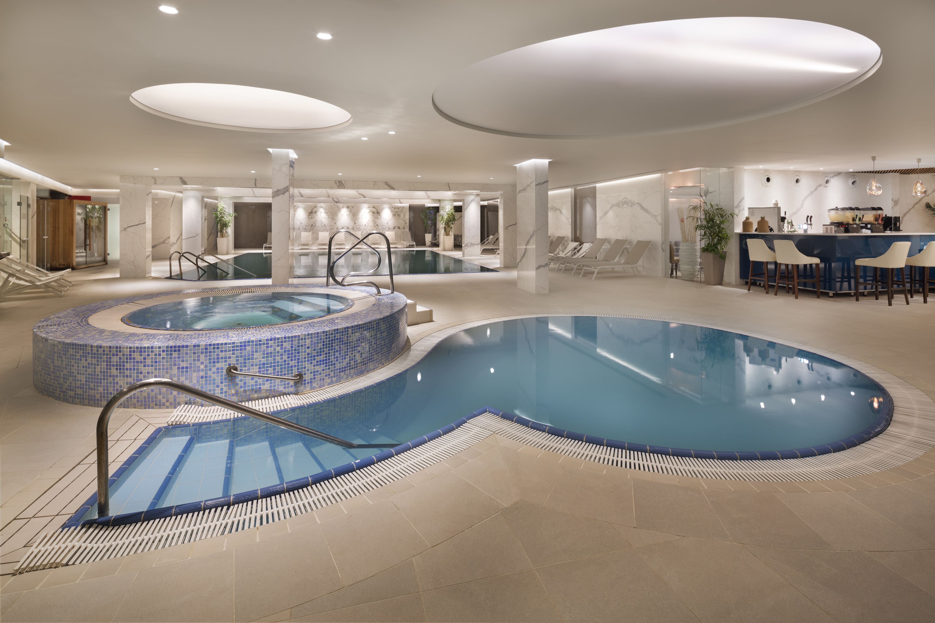 Une grande piscine intérieure dotée d’un jacuzzi, de chaises longues et d’un espace bar.