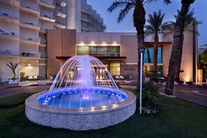 A hotel with a fountain, palm trees, and a modern building facade. - Herbert Samuel Hod Dead Sea Hotel (Tamar)