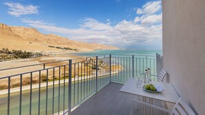 A balcony with a table, chairs, and a view of a beach and sea. - Herbert Samuel Hod Dead Sea Hotel (Tamar)
