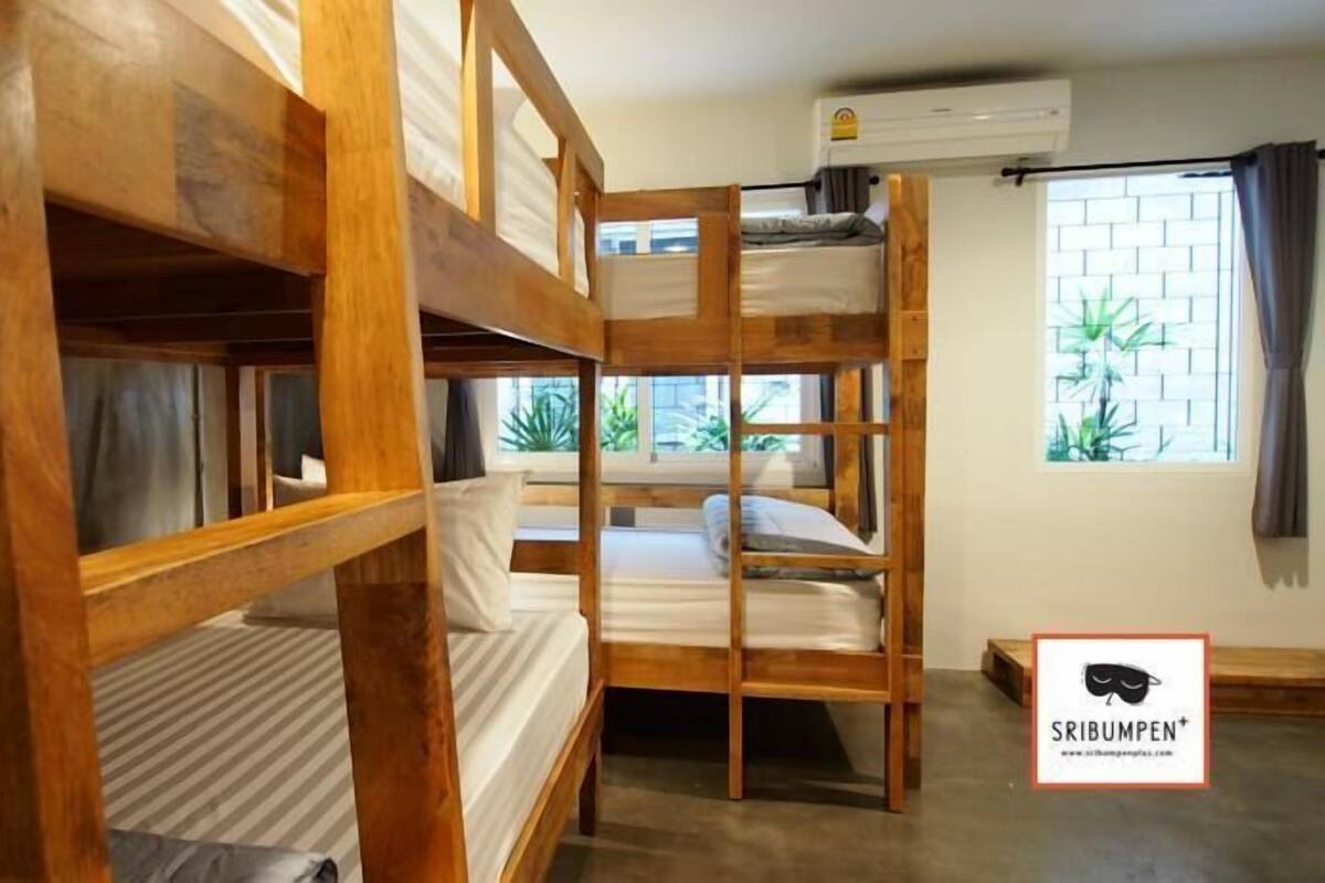 A bunk bed room with wooden frames, a window with plants, and an air conditioning unit.
