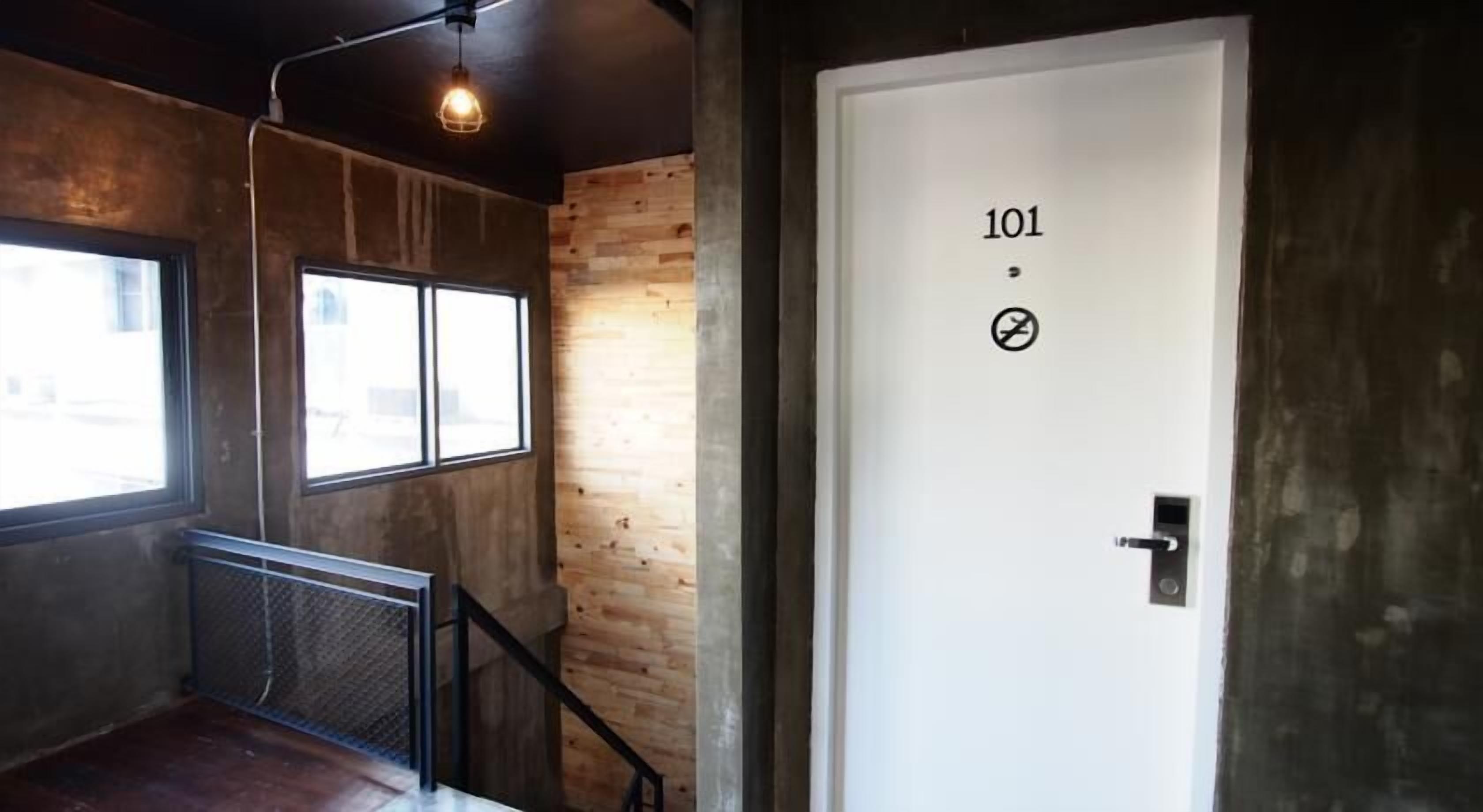 A room with a wooden floor, a window, a metal railing, and a white door with the number 101 and a symbol.