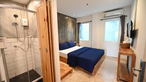 Une chambre avec une douche, un lit avec une literie bleue, une table de chevet en bois et un téléviseur fixé au mur.