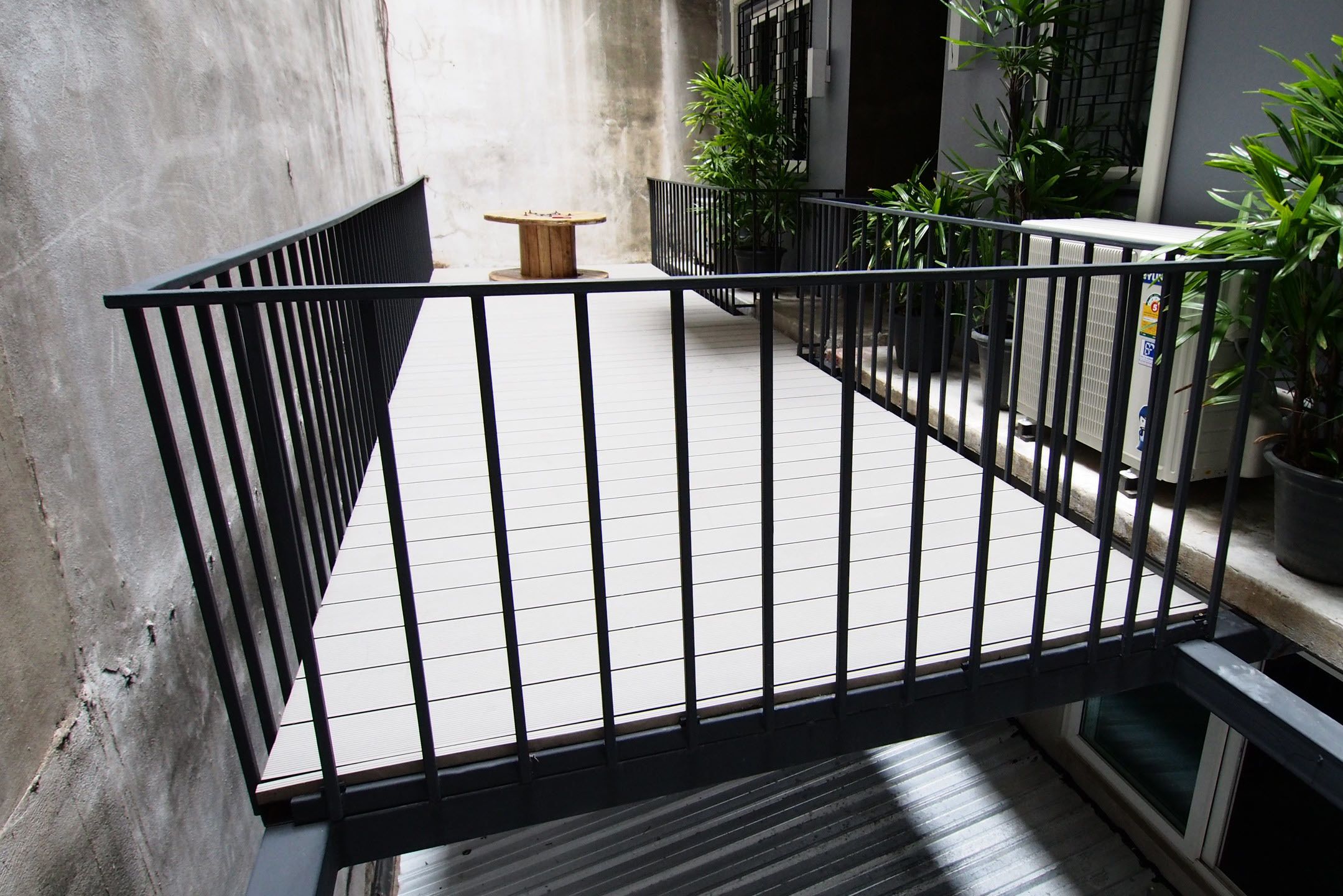 Un balcon doté d’une balustrade en métal noir, de plantes en pot et d’une petite table en bois.