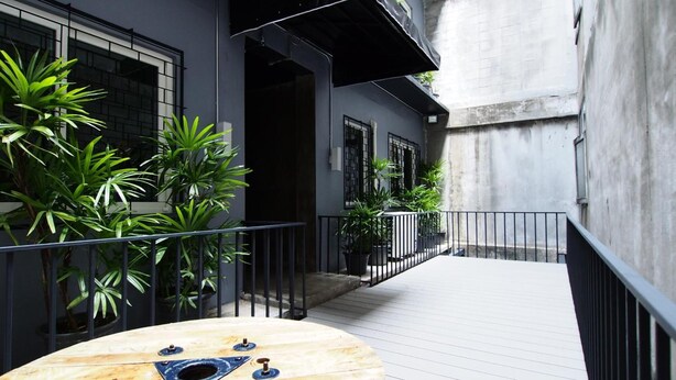 Un étroit couloir extérieur doté d’une terrasse en bois, de plantes en pot et d’une rambarde en métal.