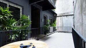 Un étroit couloir extérieur doté d’une terrasse en bois, de plantes en pot et d’une rambarde en métal.