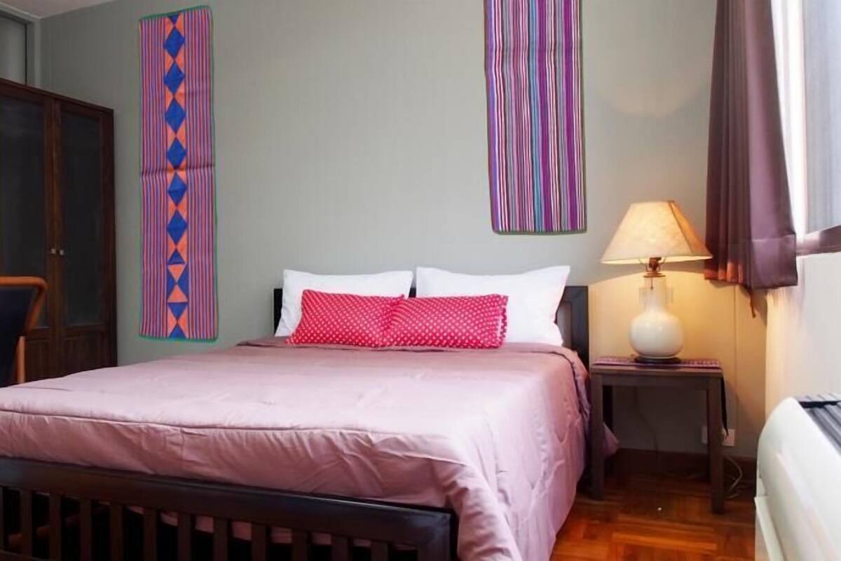 A bedroom with a bed, a chair, a wardrobe, and a nightstand with a lamp.