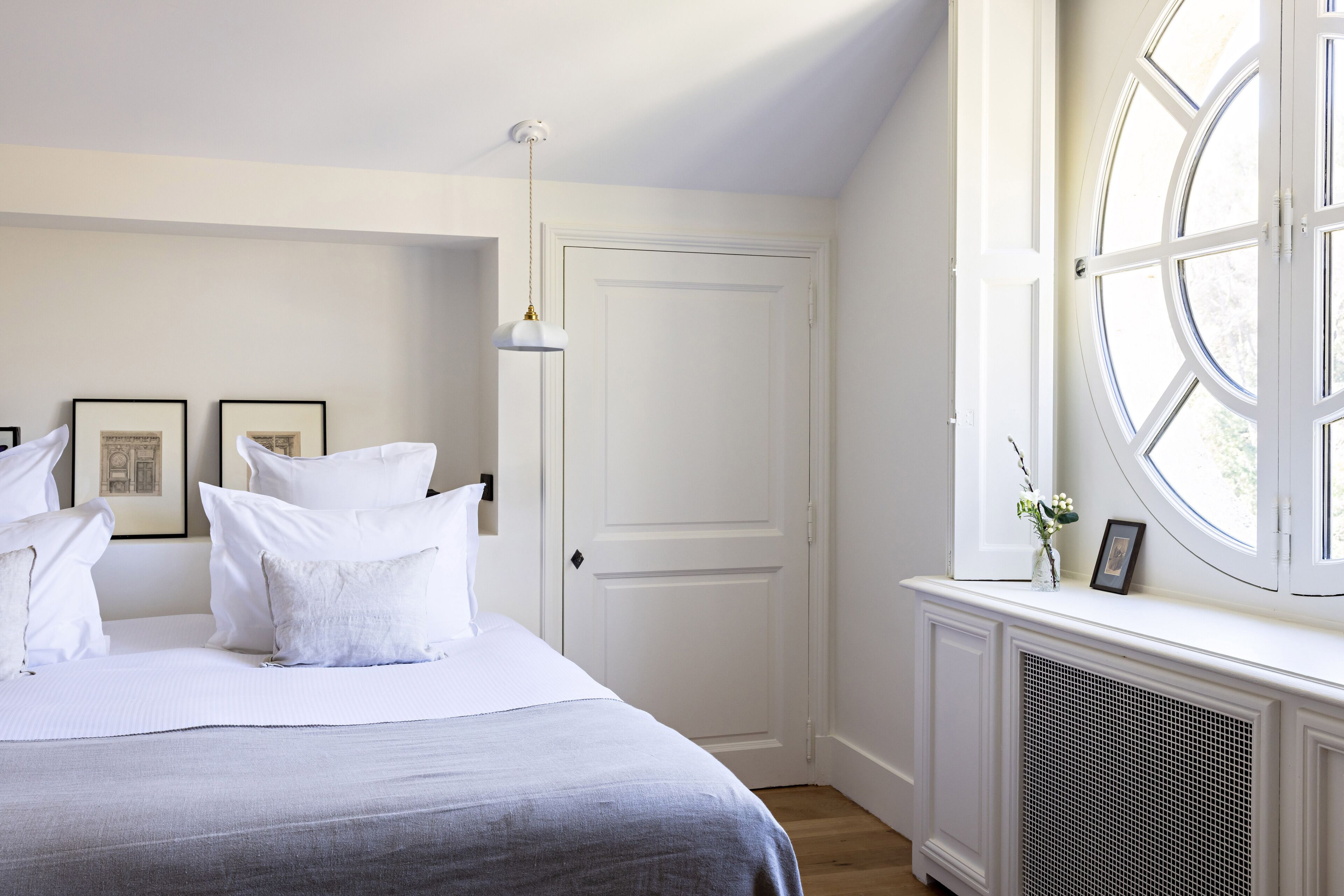 Un dormitorio con cama, paredes blancas, una puerta, una ventana y un radiador.