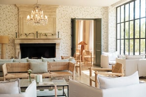 A spacious living room with a fireplace, a chandelier, and a large window. - Domaine de Fontenille - Fontenille Collection (Lauris)