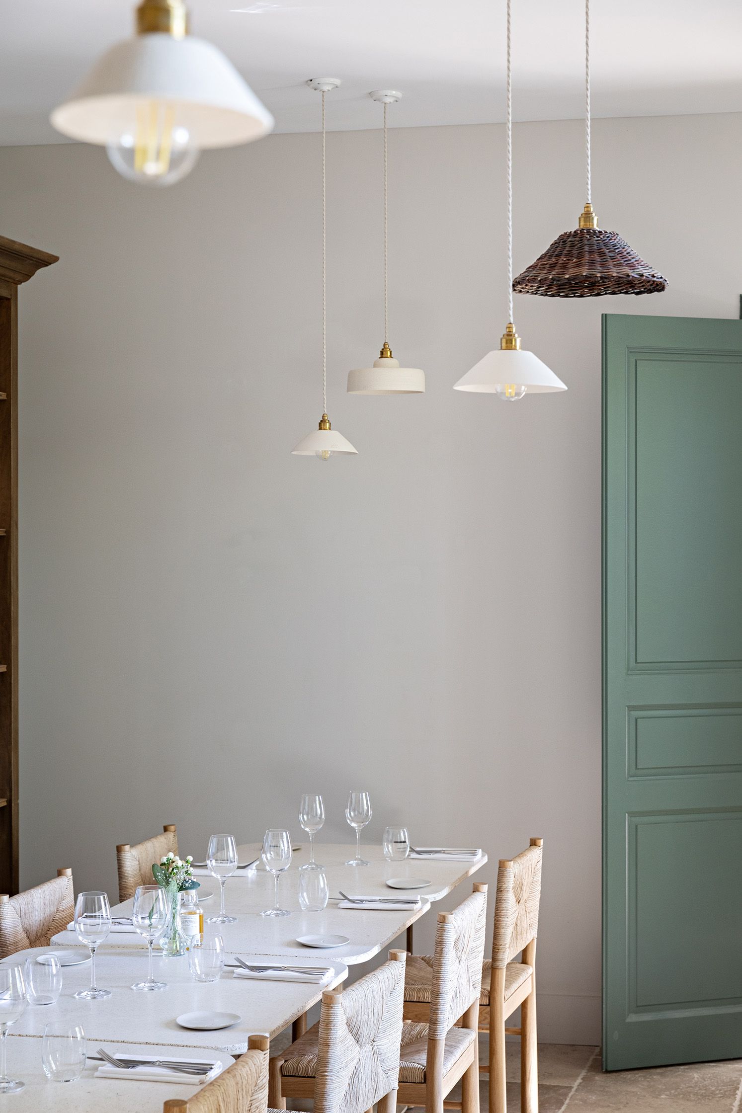 Un'area pranzo con un tavolo apparecchiato per quattro persone, sedie, lampade a sospensione e una porta verde.