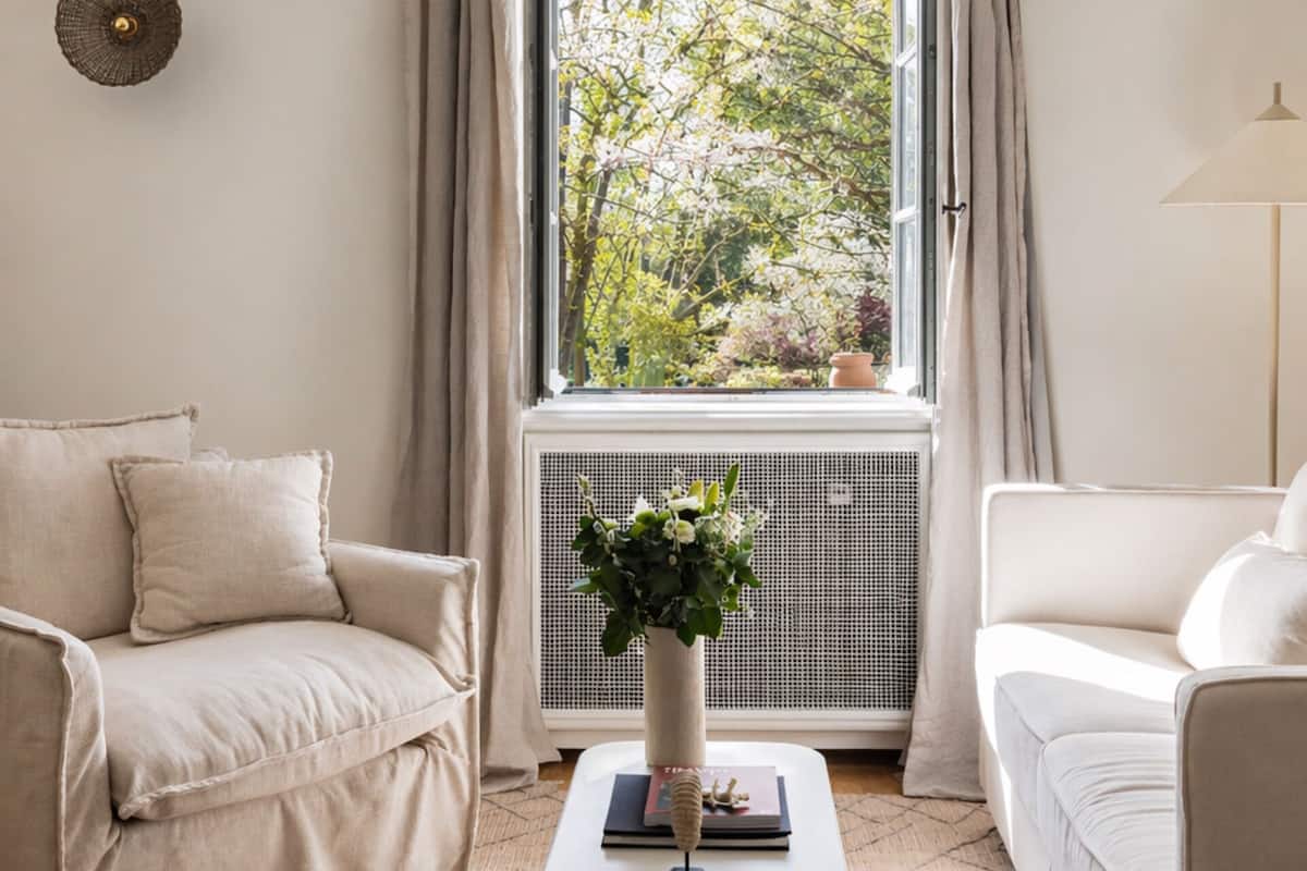 Une pièce avec un canapé blanc, une petite table sur laquelle est posée une plante, et une fenêtre avec des rideaux.