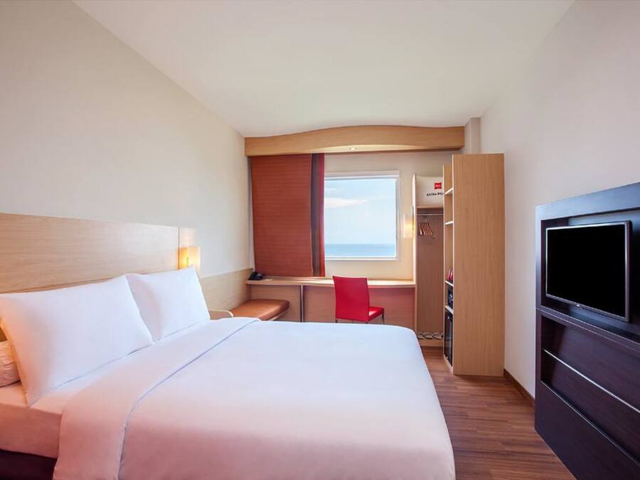 A hotel room with a large bed, a desk with a chair, a TV, and a wardrobe.