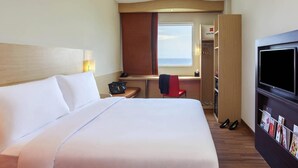 A hotel room with a bed, a desk, a chair, a TV, and a wardrobe.