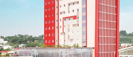 Un hôtel moderne à la façade rouge et blanche bien visible, doté d’une galerie couverte et d’un espace de stationnement.