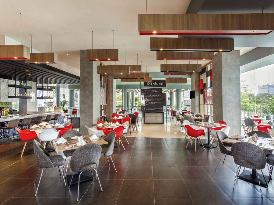A modern restaurant with a bar area, red and grey chairs, and a view of the city.