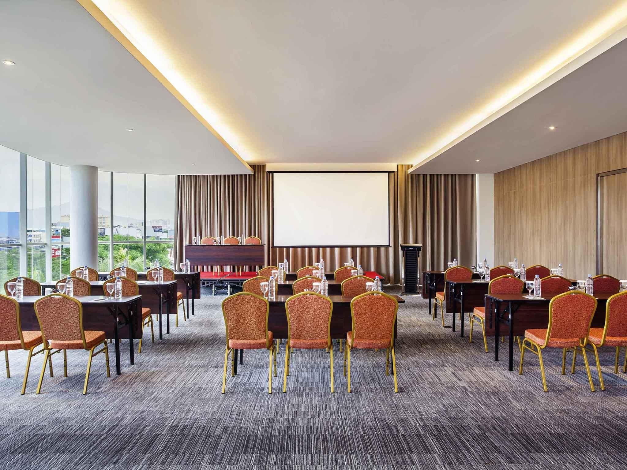 A conference room with multiple tables and chairs, a large screen, and a podium.