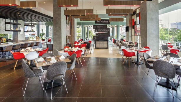 A modern restaurant with a bar area, red and grey chairs, and a view of the city.
