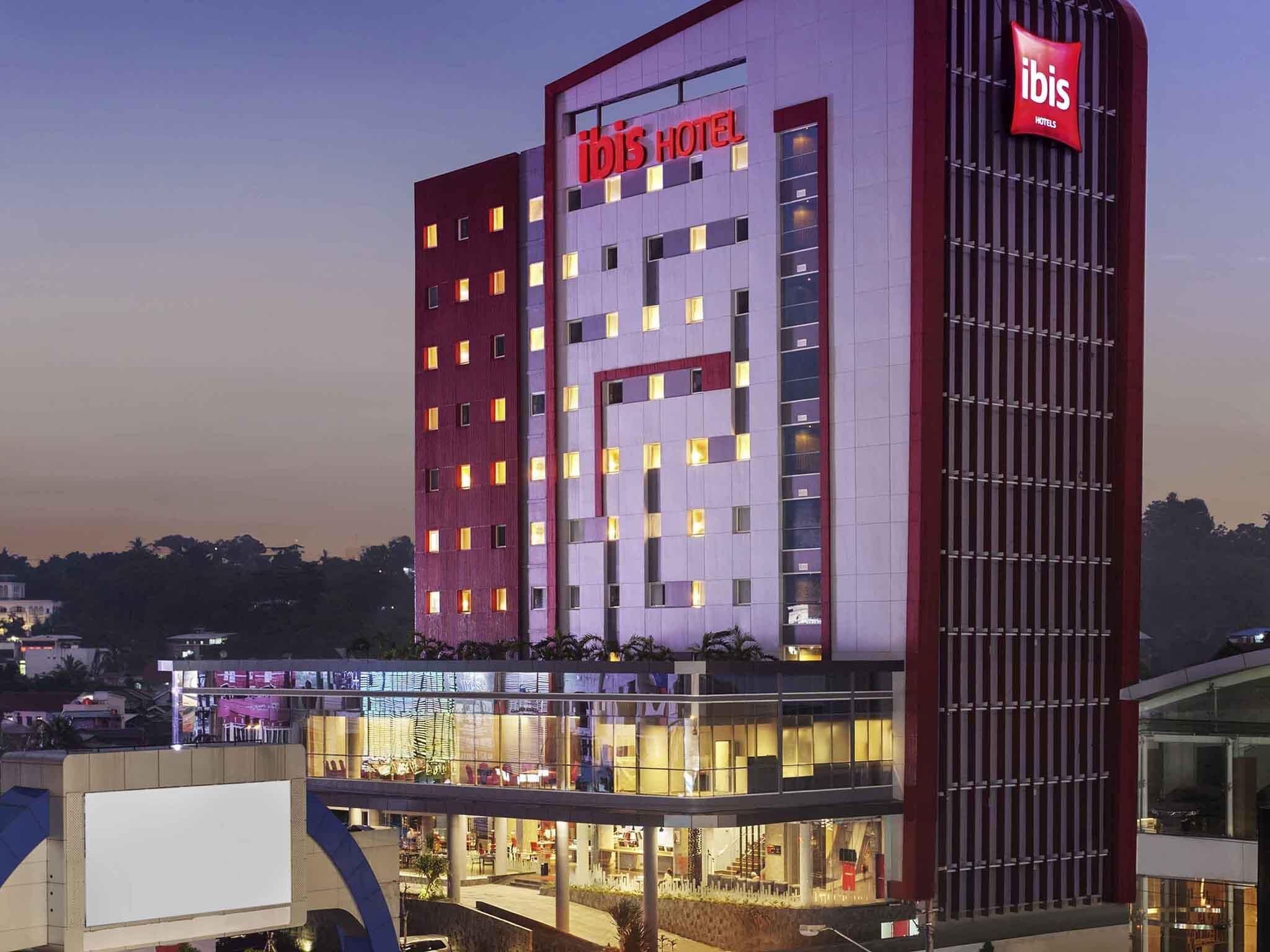 A multi-story hotel with a prominent 'ibis' sign, a glass facade, and a ground-level shopping area.