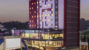 A multi-story hotel with a prominent 'ibis' sign, a glass facade, and a ground-level shopping area.