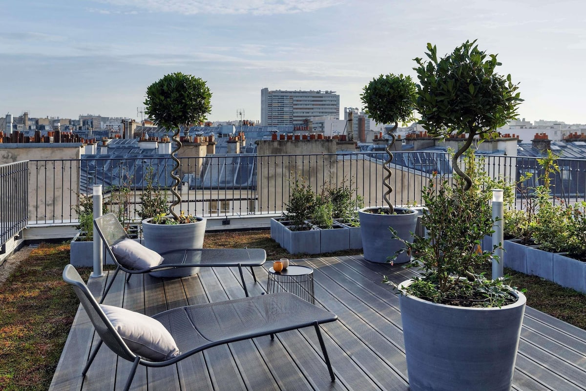 A rooftop terrace with a seating area, potted plants, and a view of the cityscape.