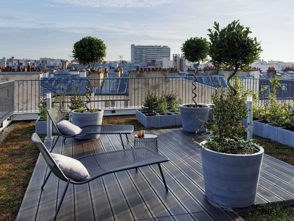 Une terrasse sur le toit, aménagée avec un espace salon, des plantes en pot et offrant une vue sur le paysage urbain.