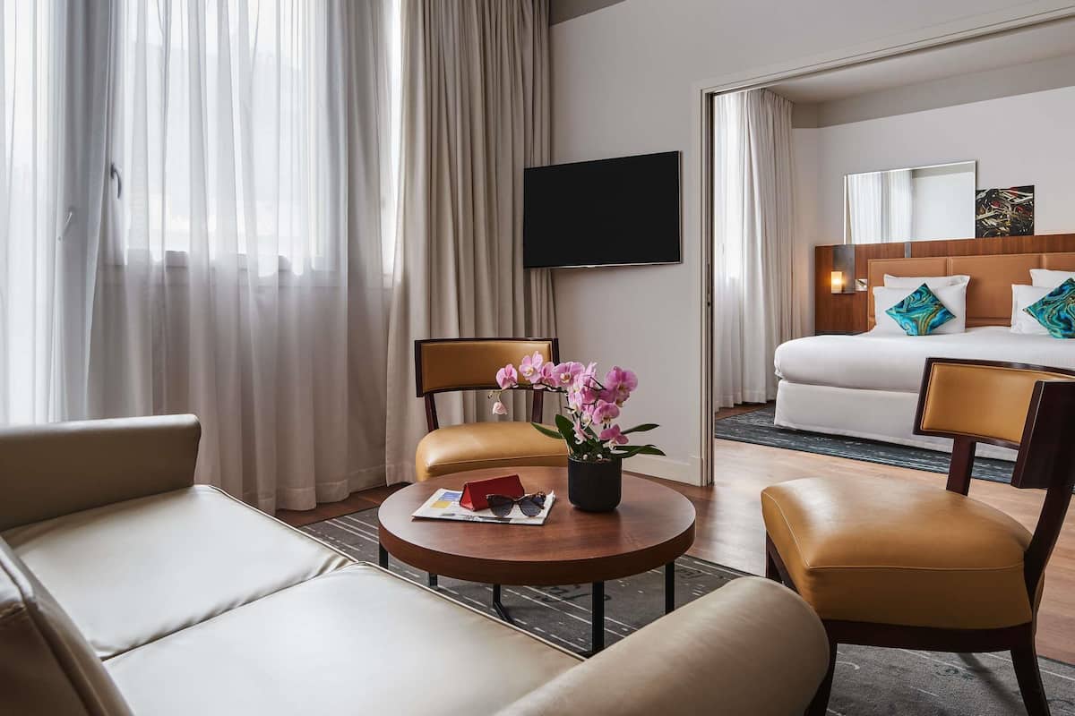 A hotel room with a bed, a TV, a desk with a chair, and a window with curtains.