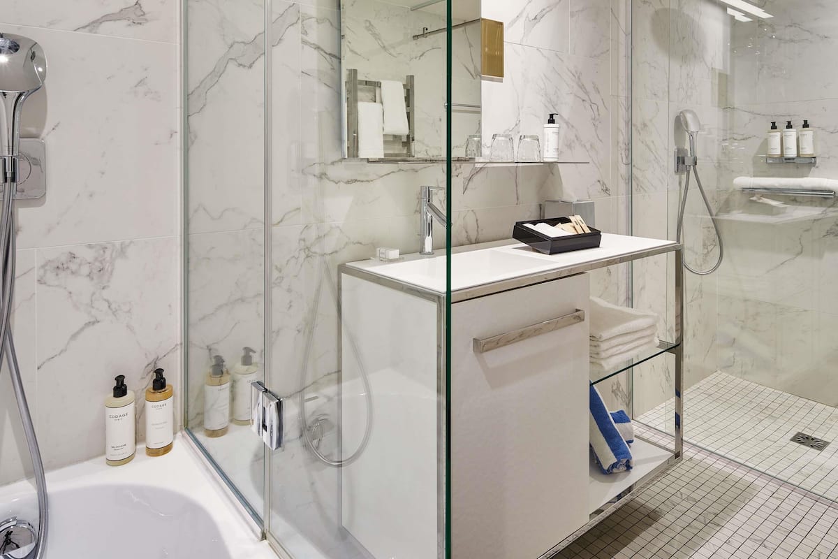 A modern bathroom with a glass-enclosed shower, a white marble sink, and toiletries on the countertop.