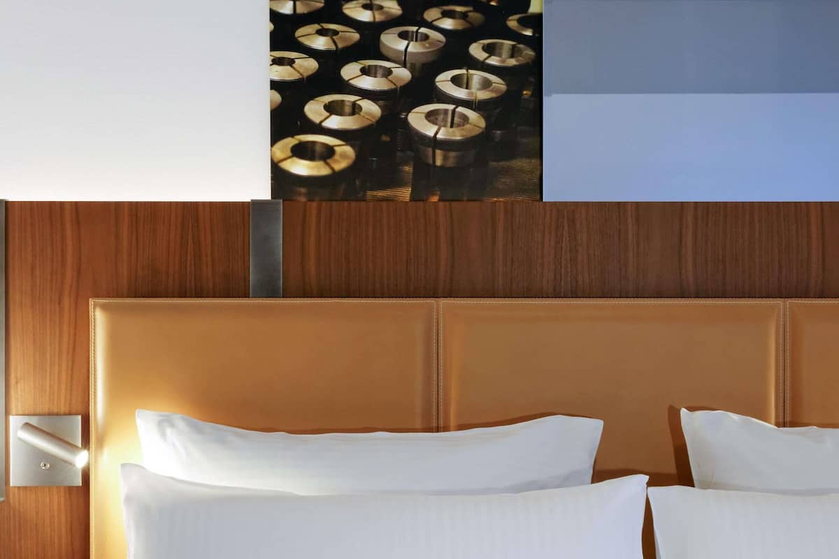 Hotellihuone, jossa on puinen pääty, kaksi valkoista tyynyä ja seinään asennettu valokytkin.