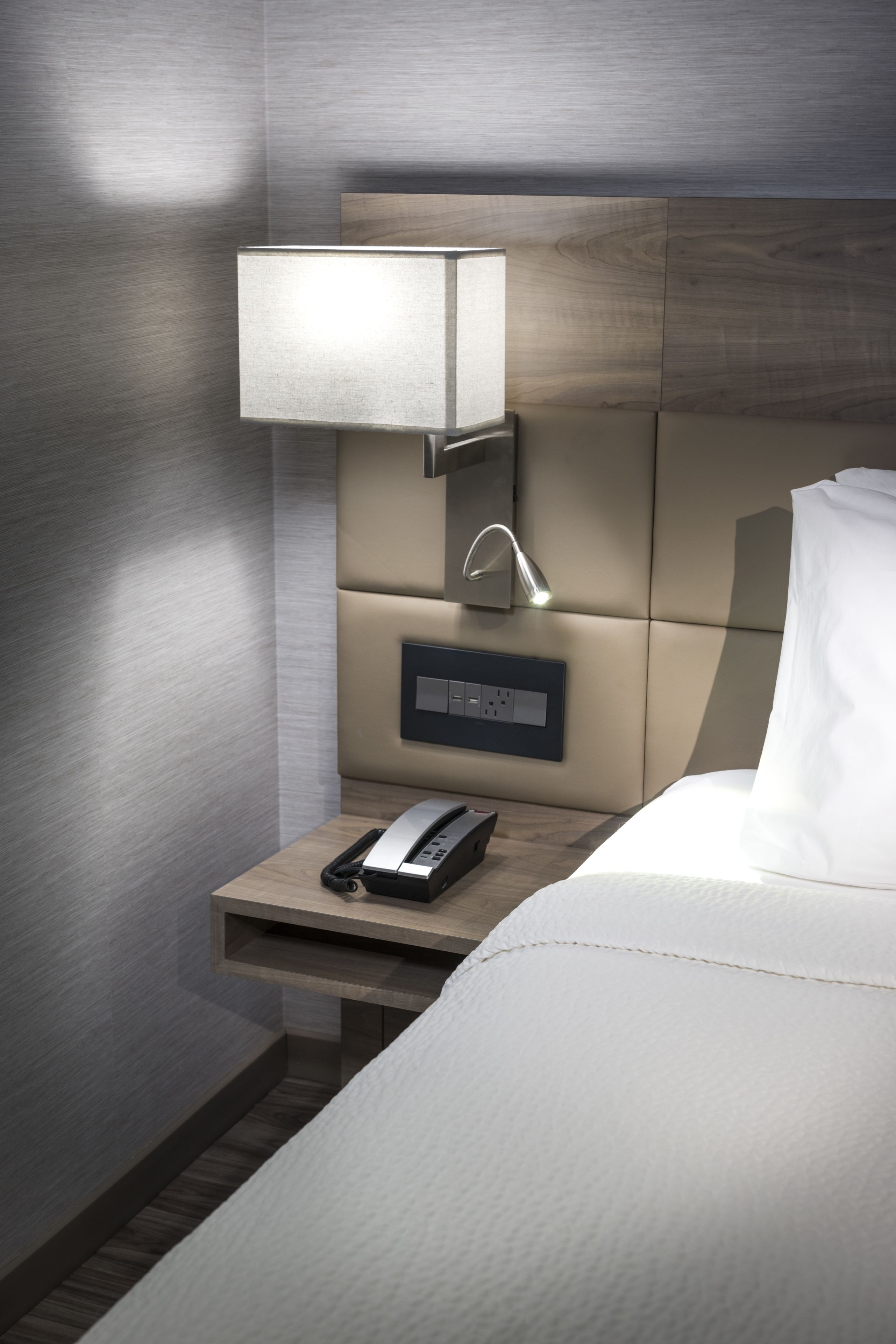 A modern hotel room with a neatly made bed, a bedside table with a lamp, and a phone.