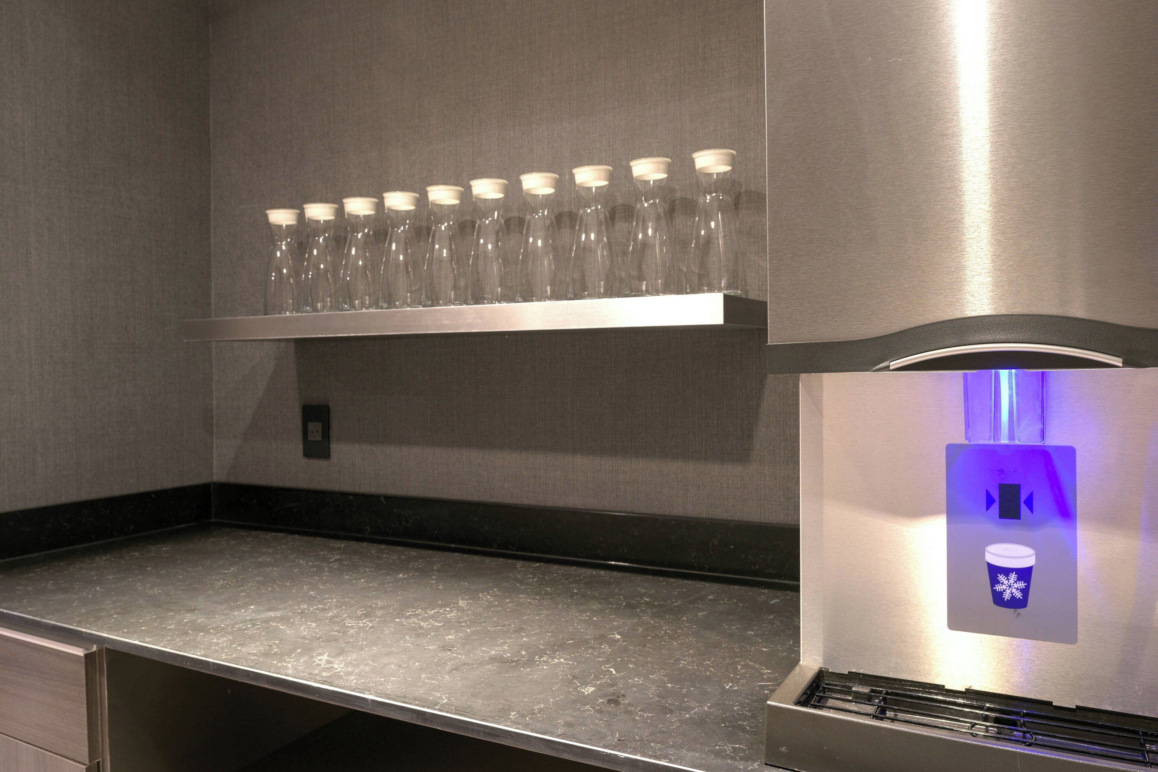 A stainless steel counter with a row of clear glasses and a coffee machine with a blue light.