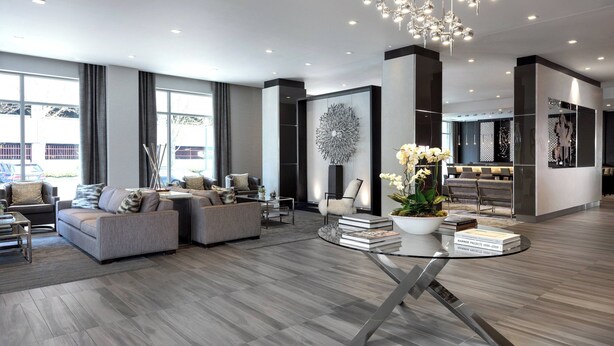 A modern living room with grey sofas, a glass coffee table, and a decorative chandelier. - AC Hotel by Marriott Boston North (Medford)