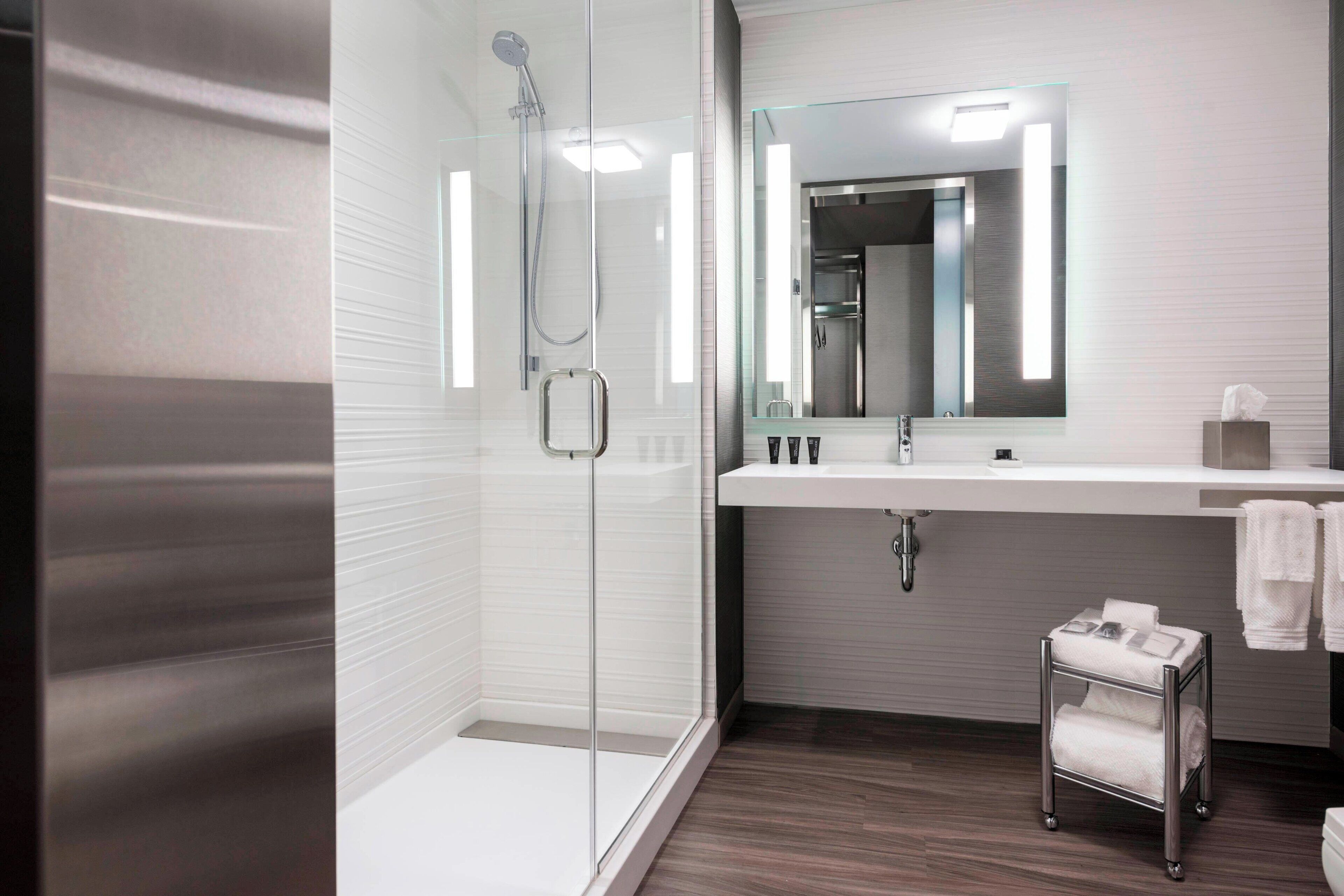 Une salle de bain moderne avec une douche à parois de verre, un meuble-lavabo avec un miroir et un petit chariot contenant des serviettes.