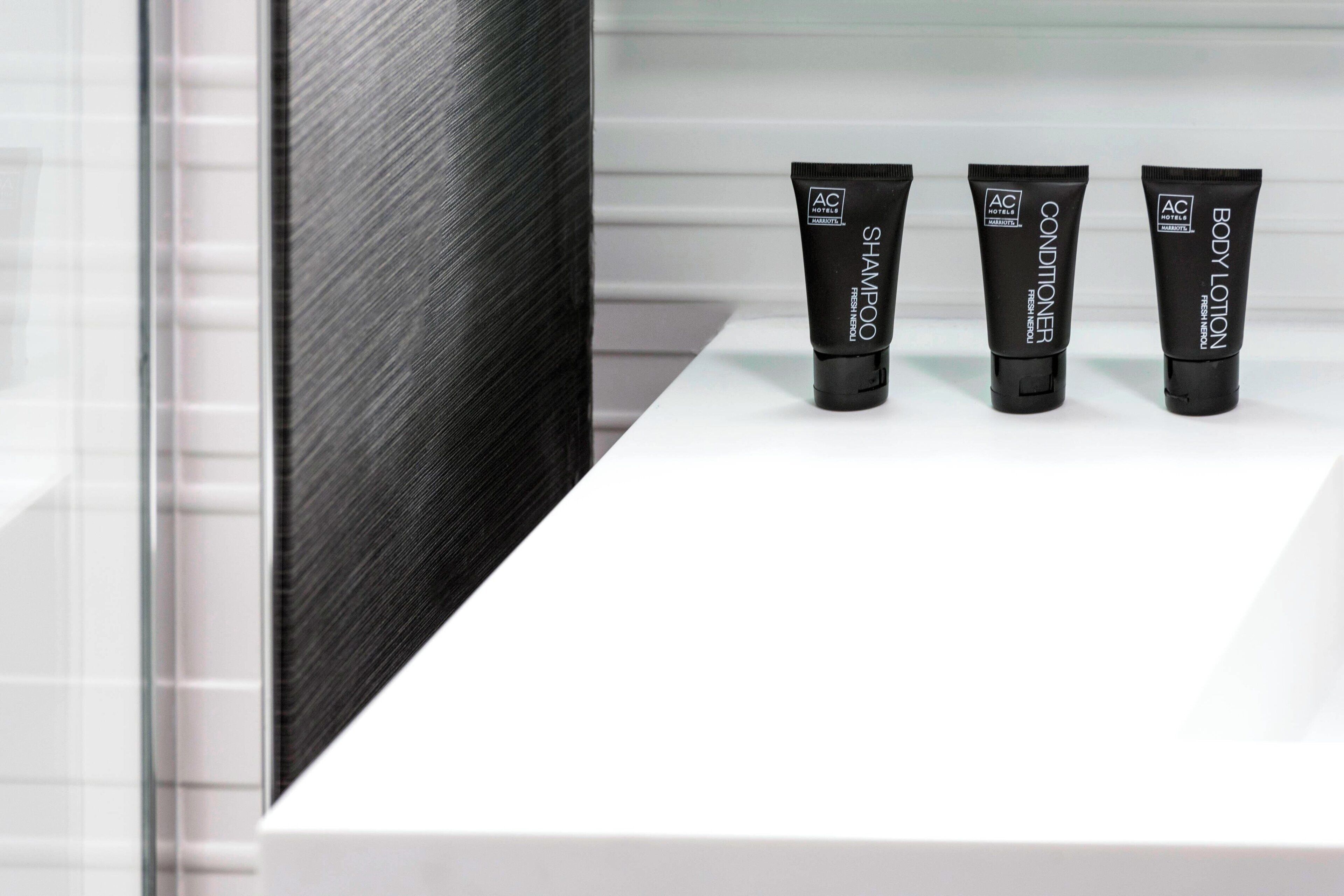 Tres tubos negros de productos Fresh & Pure de AC Hotel sobre un estante blanco.