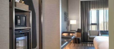 Une chambre d’hôtel équipée d’un minibar, d’un bureau avec une chaise, d’un canapé et d’un lit.