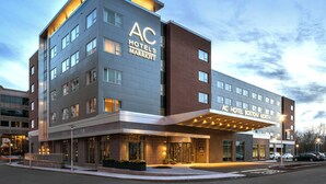 A modern hotel with a prominent AC logo, large windows, and a well-lit entrance. - AC Hotel by Marriott Boston North (Medford)