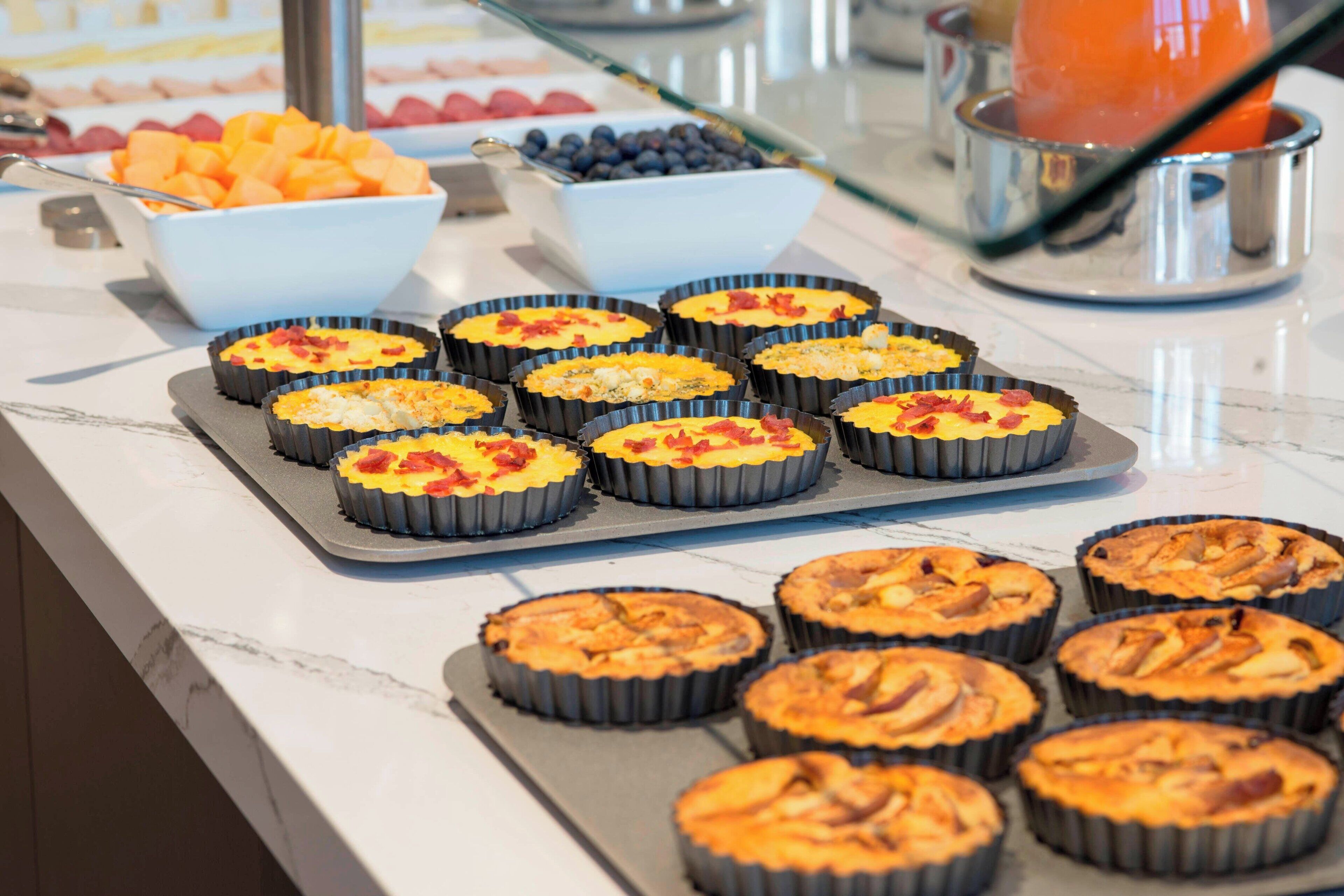 Un buffet proposant une variété d’aliments, notamment des fruits, des pâtisseries, et un distributeur de boissons.