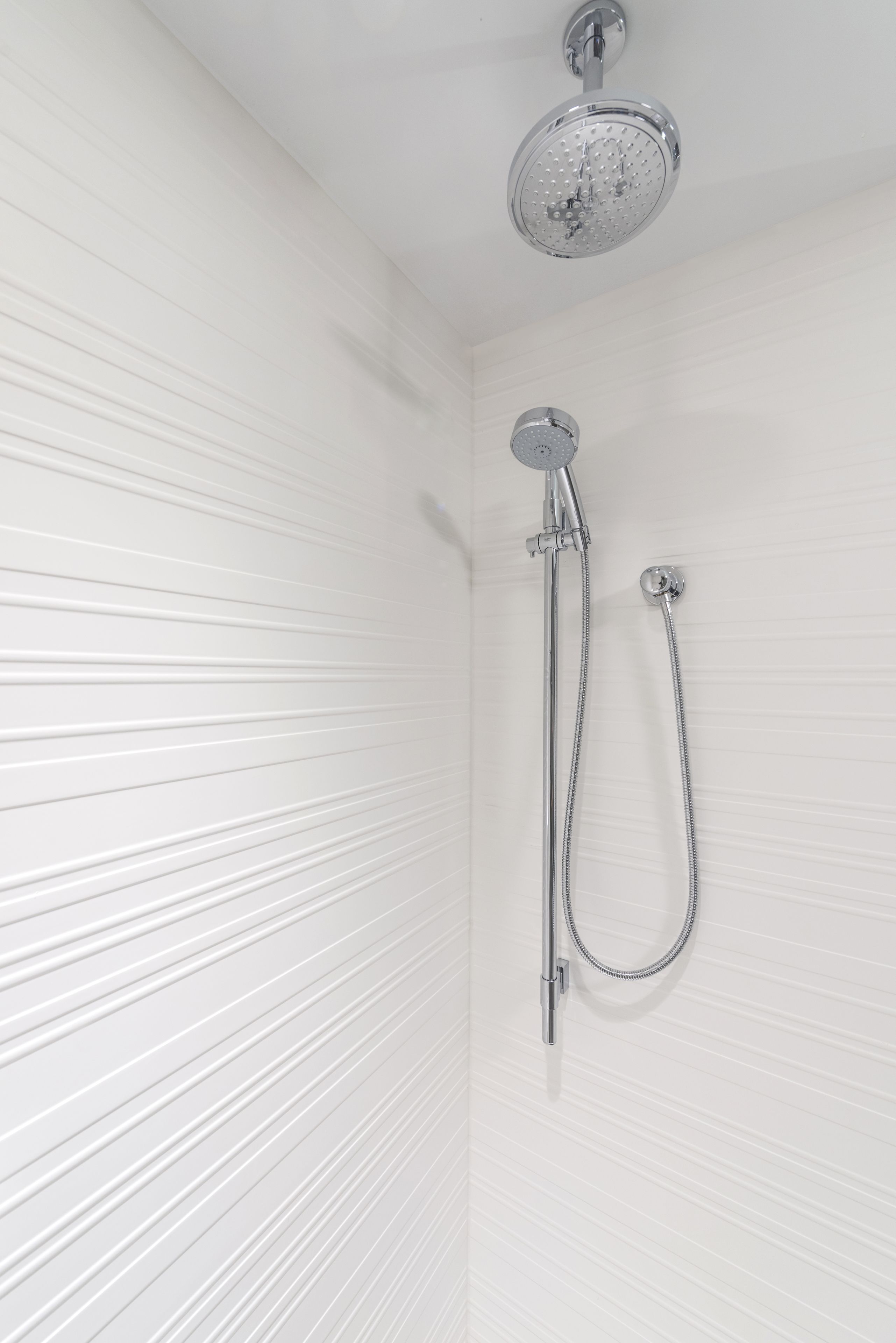A shower with a handheld showerhead and a fixed showerhead on a white tiled wall.