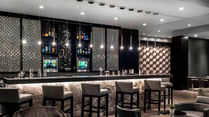 A modern bar area with a marble countertop, bar stools, and a variety of liquor bottles. - AC Hotel by Marriott Boston North (Medford)