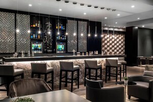 Zona de bar moderna con mostrador de mármol, taburetes y una variedad de botellas de licor.