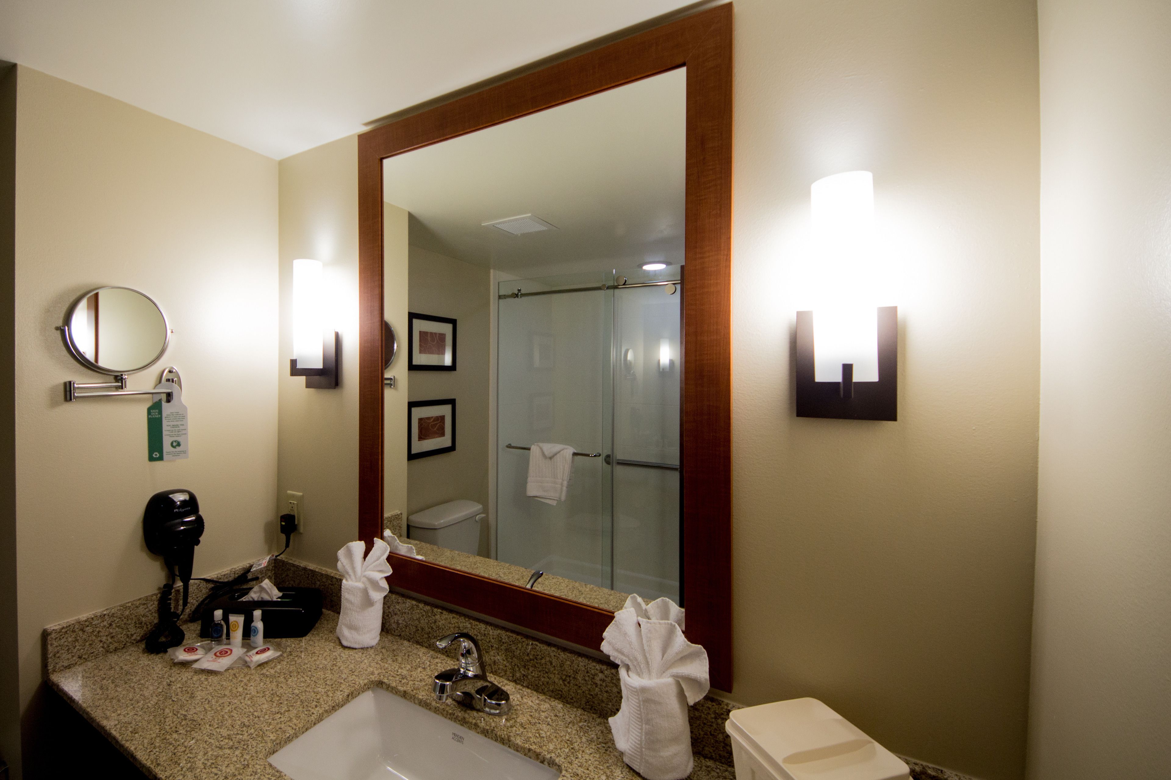 A hotel bathroom with a large mirror, a sink, a hairdryer, and a towel rack.