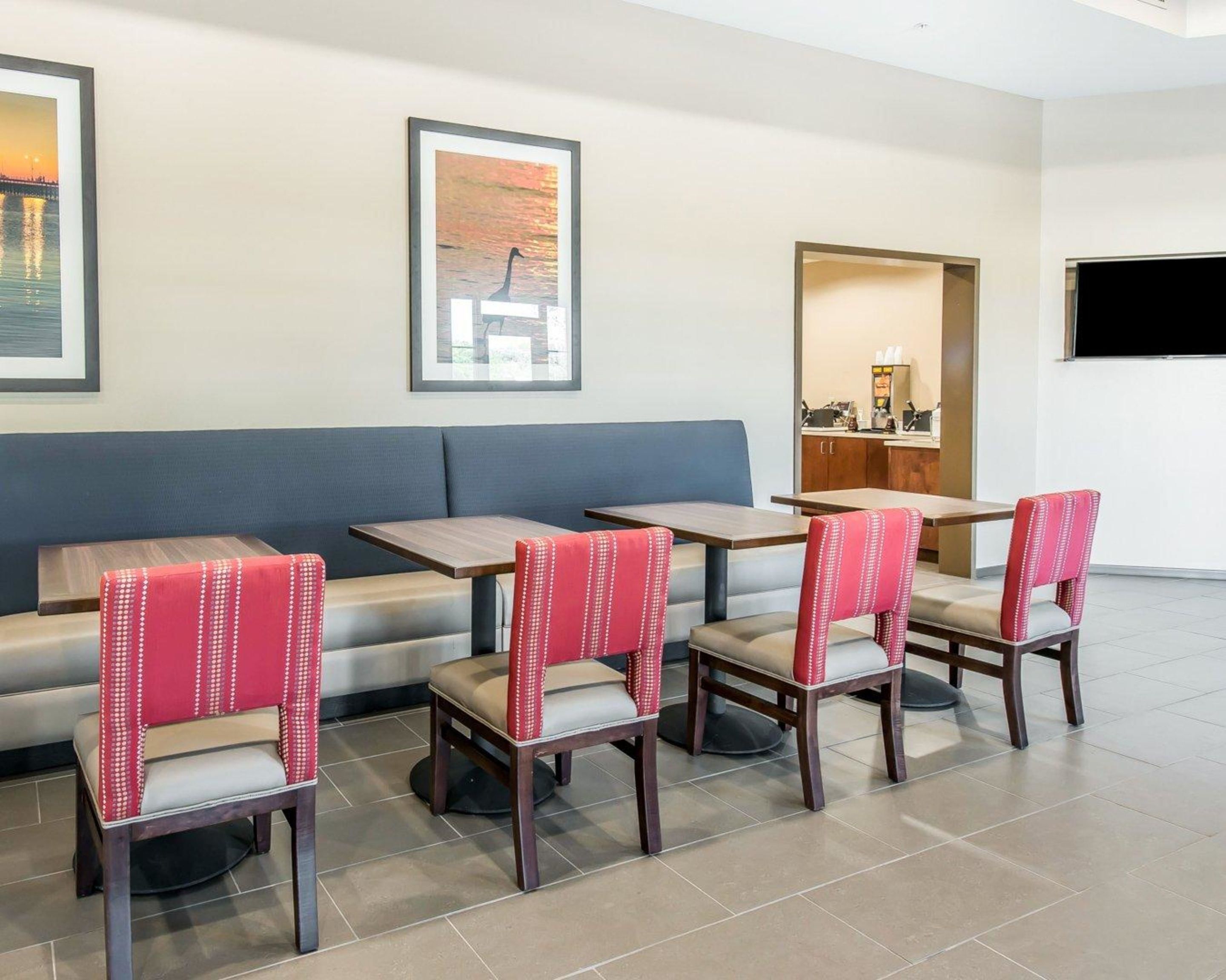 A hotel lobby with a blue sofa, four wooden tables, and red upholstered chairs.