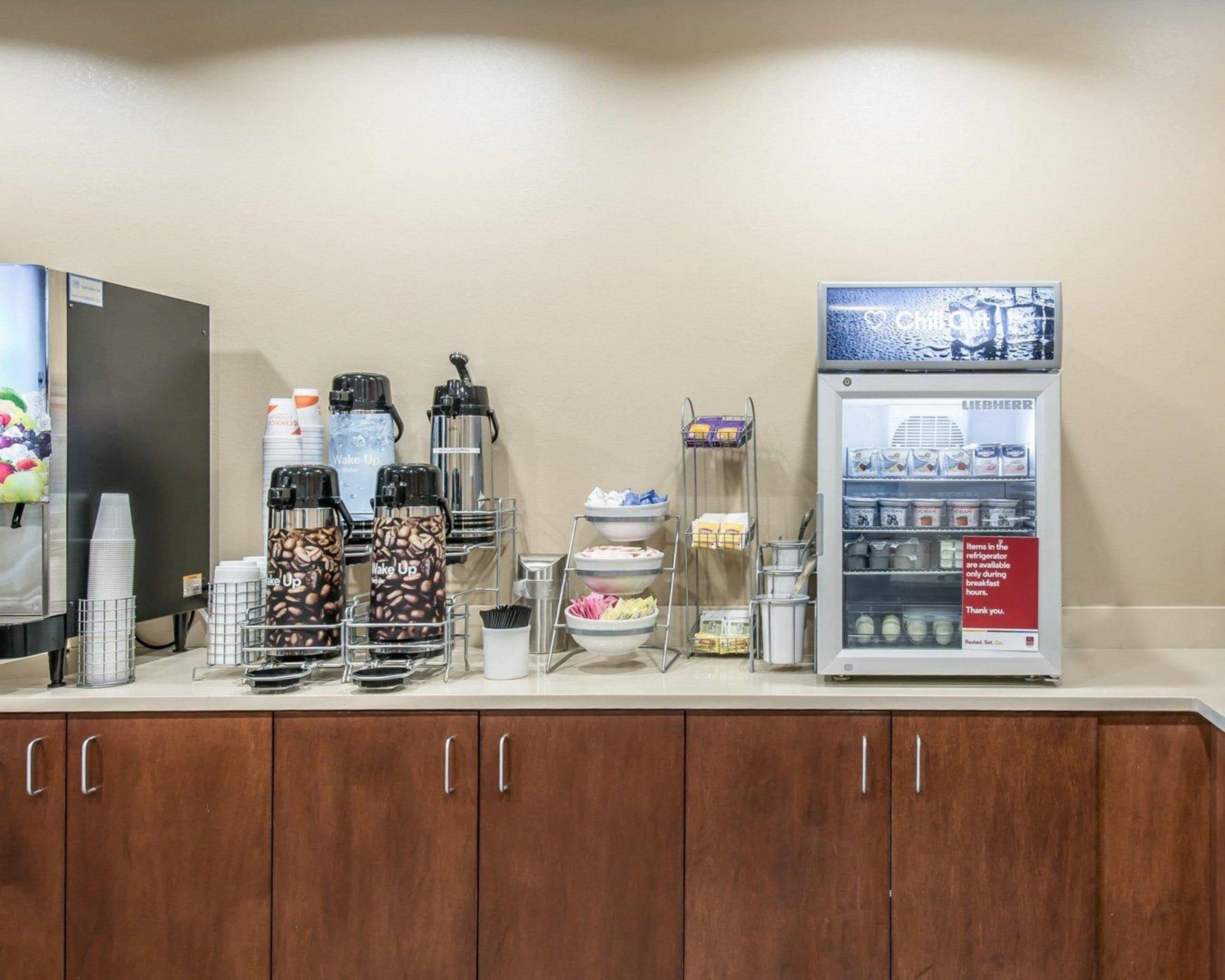 Uma cozinha compacta com cafeteira, geladeira abastecida com itens de café da manhã e dispensador de café.